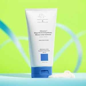 Masque méga-hydratant Silkamino posé sur une surface turquoise, sur fond vert fluo avec motif bleu incurvé. Une partie de la texture est versée à côté et devant la bouteille.