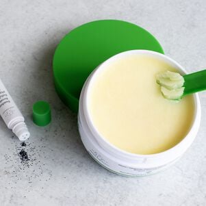 Photo d'un pot de Slaai ouvert avec la cuillère qui vient avec plongée dans le produit et un flacon de Bamboo Booster ouvert avec ses contenants se déversant sur une surface grise
