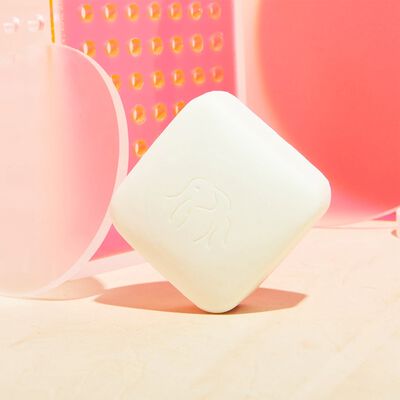 A Pekee Bar tipped against a pink background with other cleansing products behind it