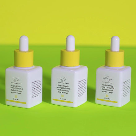 photo de trois bouteilles d'huile de marula alignées sur une surface vert clair sur fond jaune