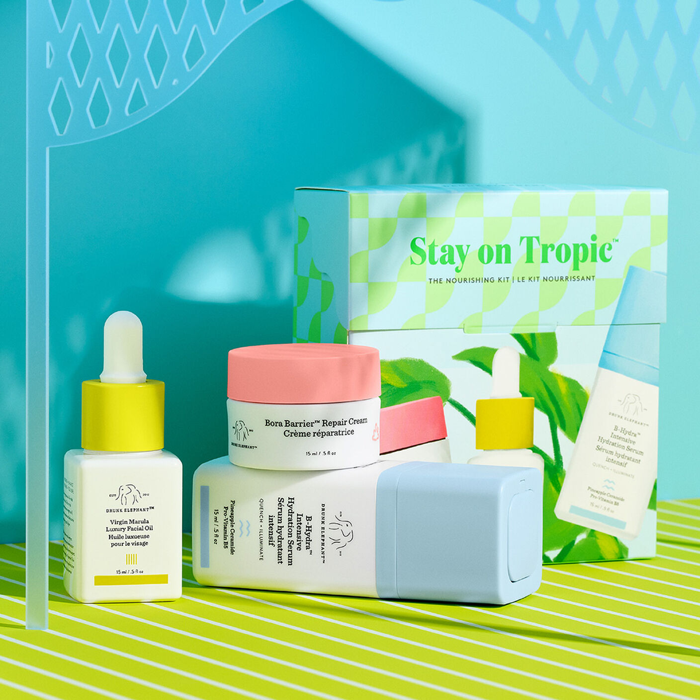 Produits Bora Barrier, B-Hydra et huile Virgin marula posés à plat devant la trousse sur une table à rayures vertes et un fond bleu