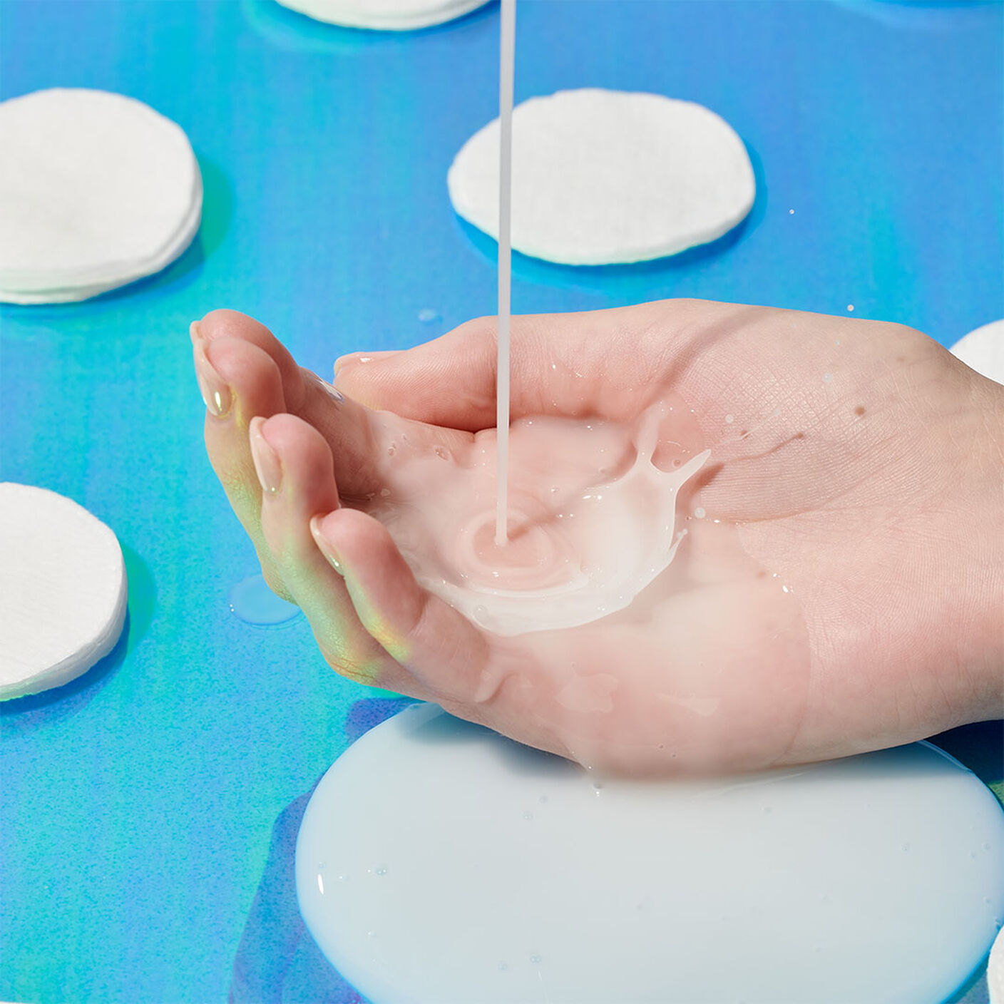 E-Rase Milki Micellar Water being poured into the palm of a hand surrounded by cotton pads. 