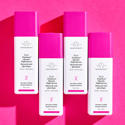 photo de quatre flacons de TLC Framboos alignés à différentes hauteurs sur un fond rose foncé