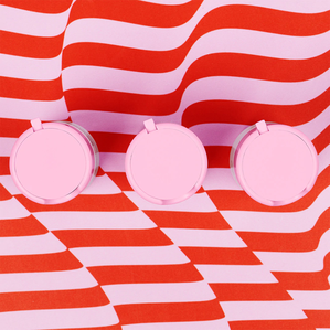 photo of three Babyfacial pump bottles viewed from the top down upon a wavy pink and red striped surface