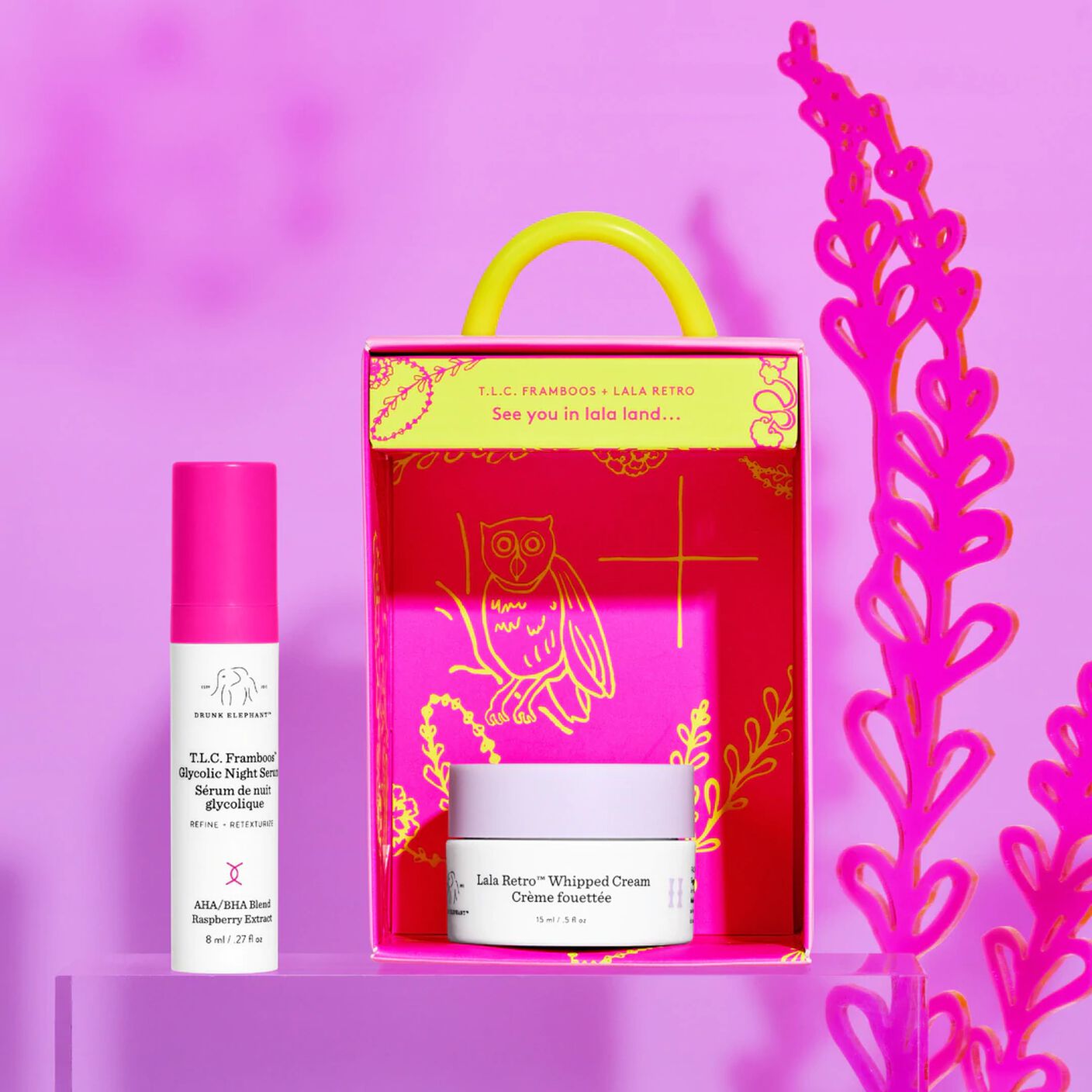 T.L.C Framboos (8ml) on a clear acrylic prop and Lala Retro (15ml) inside the pink packagaing  in front of pink floral prop. 