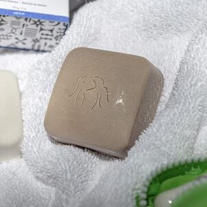 photo d'un pain nettoyant Juju Bar dans une serviette en tissu éponge blanc avec d'autres produits de nettoyage Drunk Elephant sur les bords