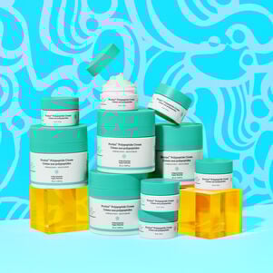 photo of multiple Protini full size and littles contatiners stacked on top of each other, one open showing teh cream, some sitting on acryclic boxes, all against a designed blue background