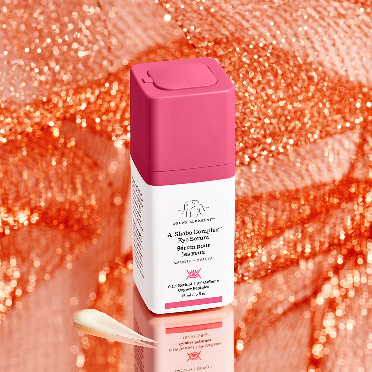 Sérum pour les yeux A-Shaba Complexe devant un fond orange brillant à côté d'une goute de produit,
