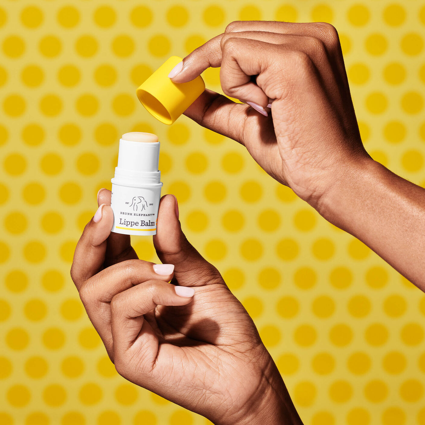 Lippe Balm held in one hand taking off the cap with the other. 